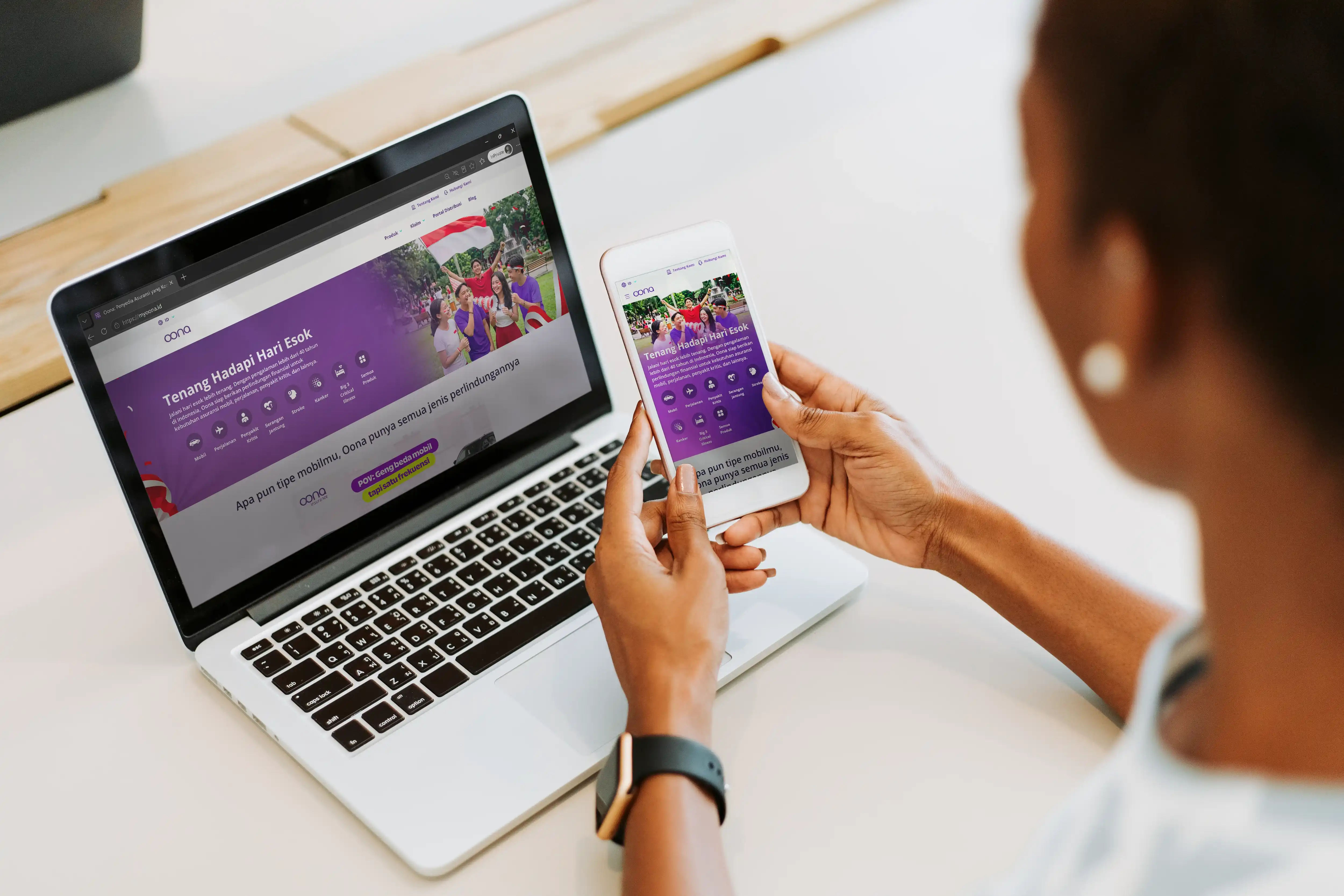 Seseorang menggunakan laptop dan smartphone untuk mengakses situs Oona Insurance